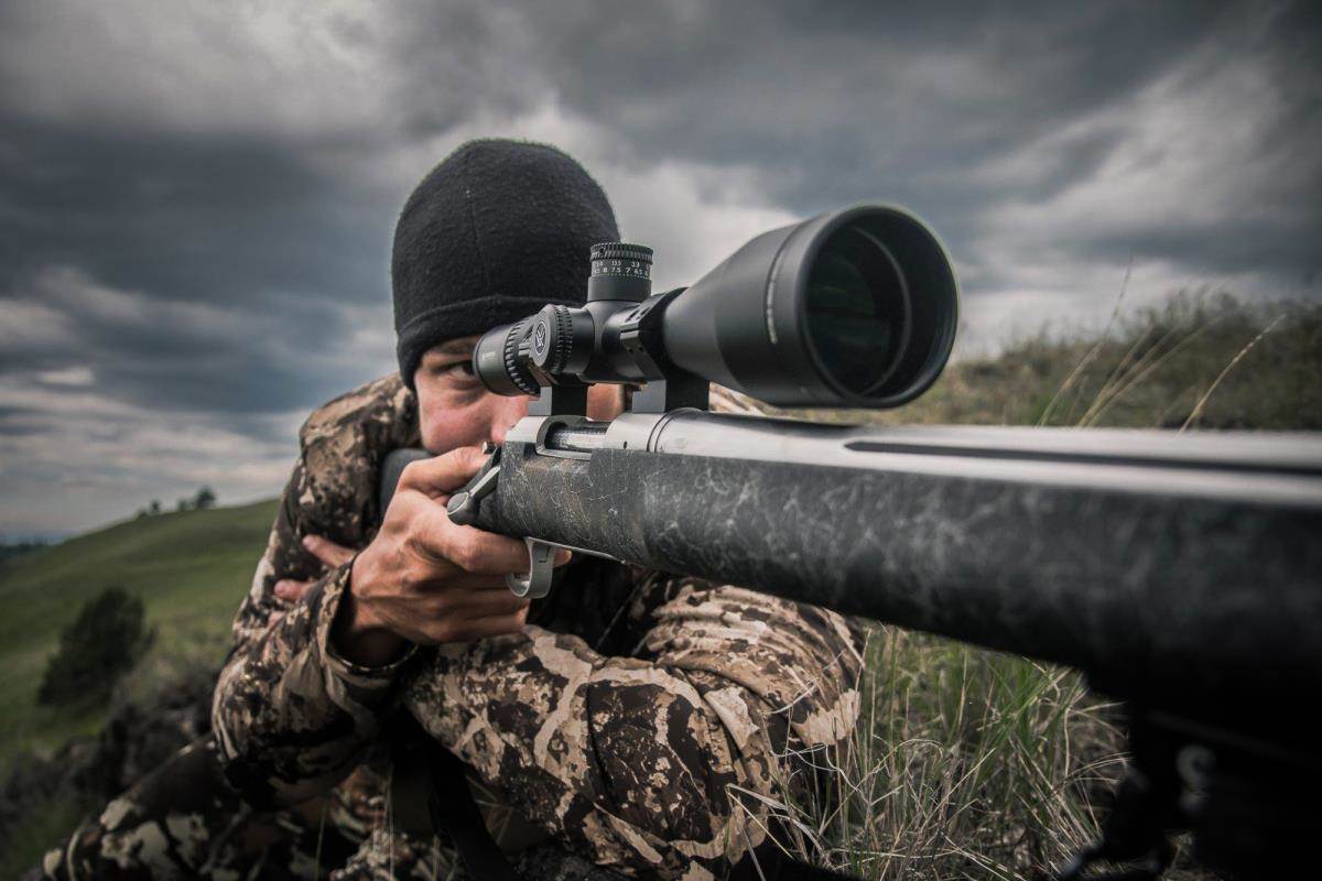 Person in camouflage clothing with a rifle and scope in a natural setting
